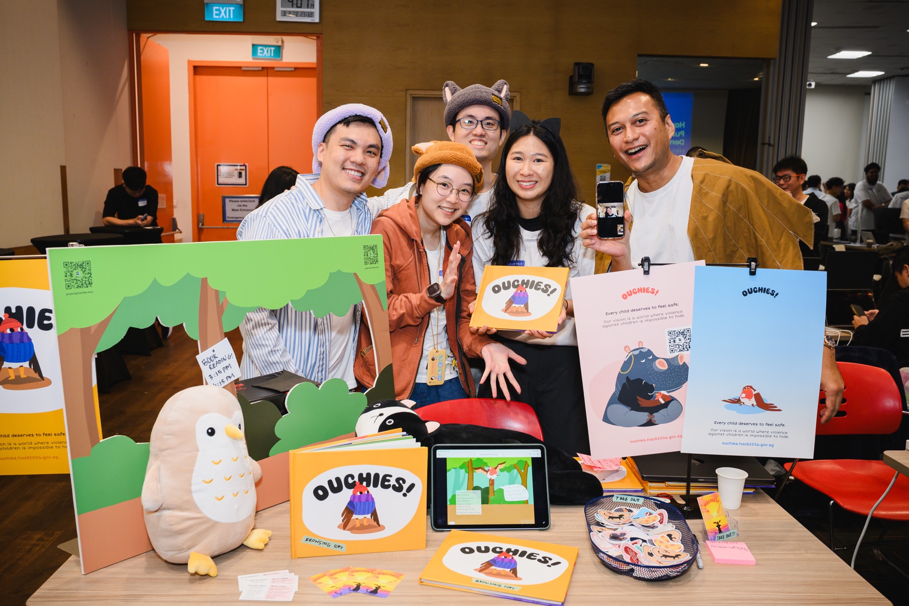 The Ouchies! team at their hackathon showcase booth, holding copies of the book and props.